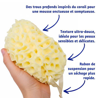 Éponge de bain « gommage corail » tenue à la main, avec un texte décrivant ses caractéristiques sur fond blanc.