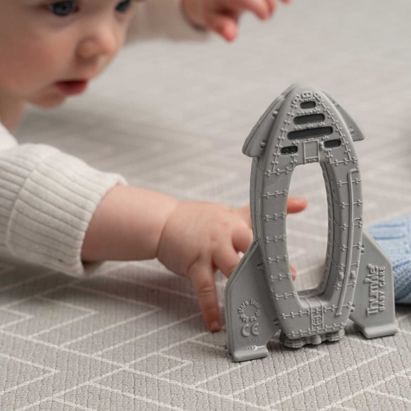 Baby on a playmat during tummy time reaching for a rocket shaped baby toy